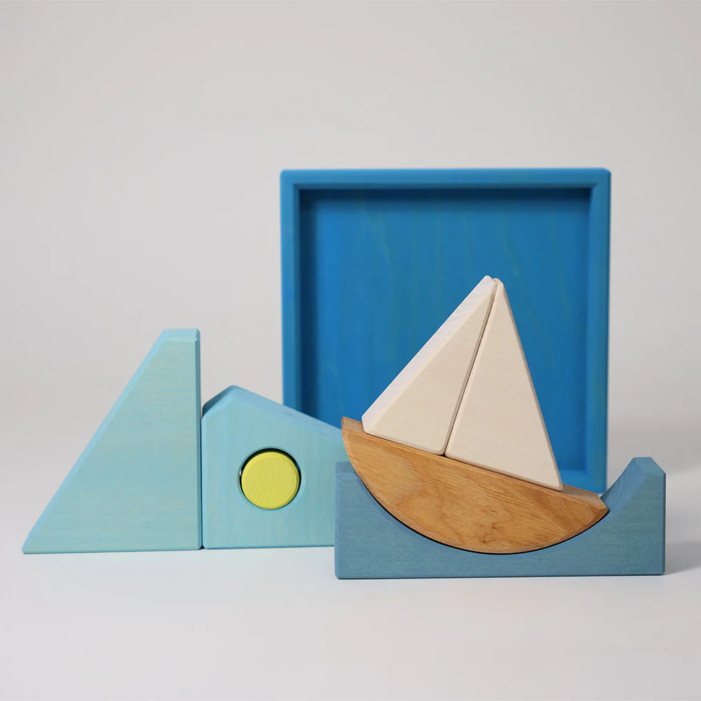 Grimm's Building Set - Blue features colorful wooden blocks arranged as a sailboat and geometric shapes in blue, white, yellow, and natural tones—a vibrant toddler toy displayed on a plain white background.