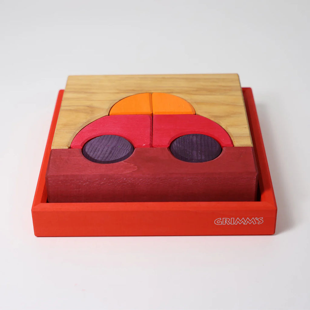 The Grimm's Building Set - Red is a colorful wooden puzzle with geometric pieces in red, purple, orange, and natural wood that form a car shape inside a red tray—perfect for creative wooden toy fans.