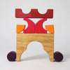 The Grimm's Building Set - Red forms a colorful structure with a natural wood arch base, red and orange blocks, two purple cylinder wheels, and a red crown shape on top, all set against a plain background.