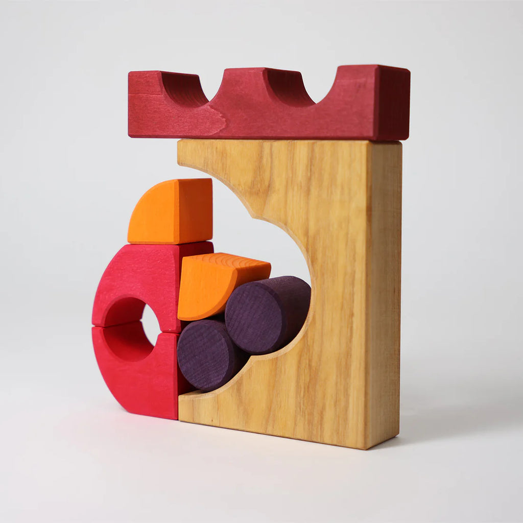 The Grimm's Building Set - Red showcases colorful wooden blocks in red, yellow, orange, and purple, featuring geometric shapes like circles and arches stacked vertically against a plain white background.