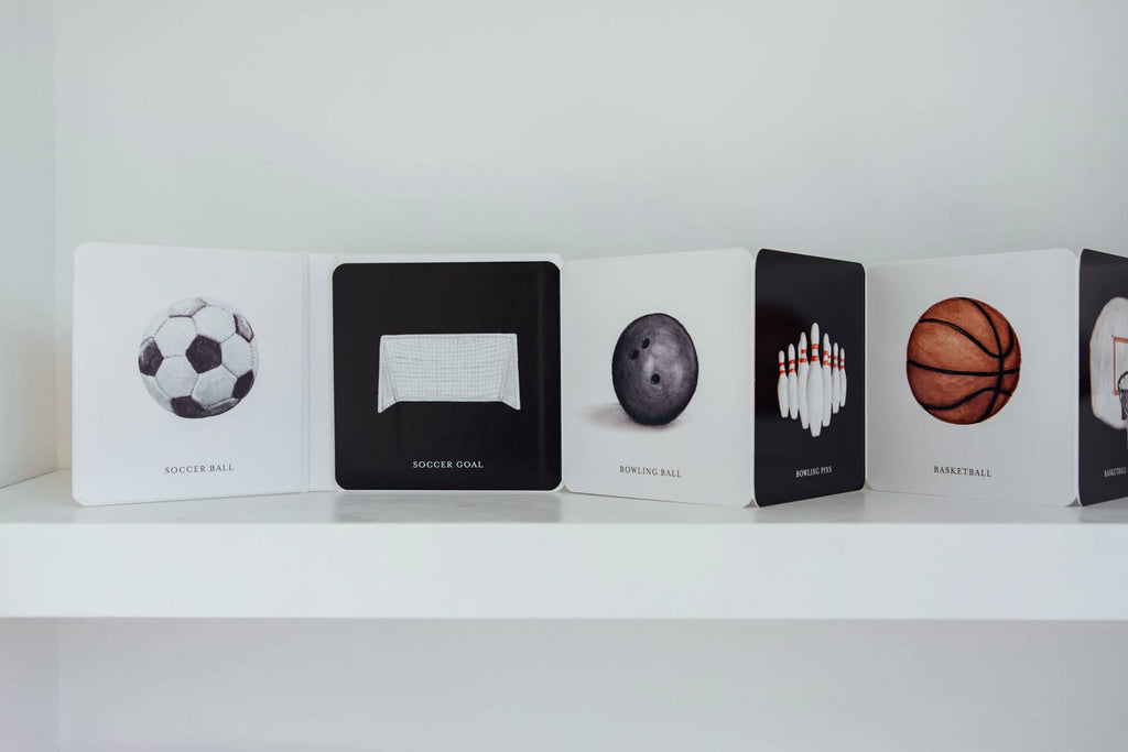 Baby's Tummy Time Sports features illustrated flashcards displayed on a white shelf, providing visual stimulation with images of a soccer ball, soccer goal, bowling ball, bowling pins, basketball, and basketball hoop—perfect for tummy time or pairing with a high-contrast board book.