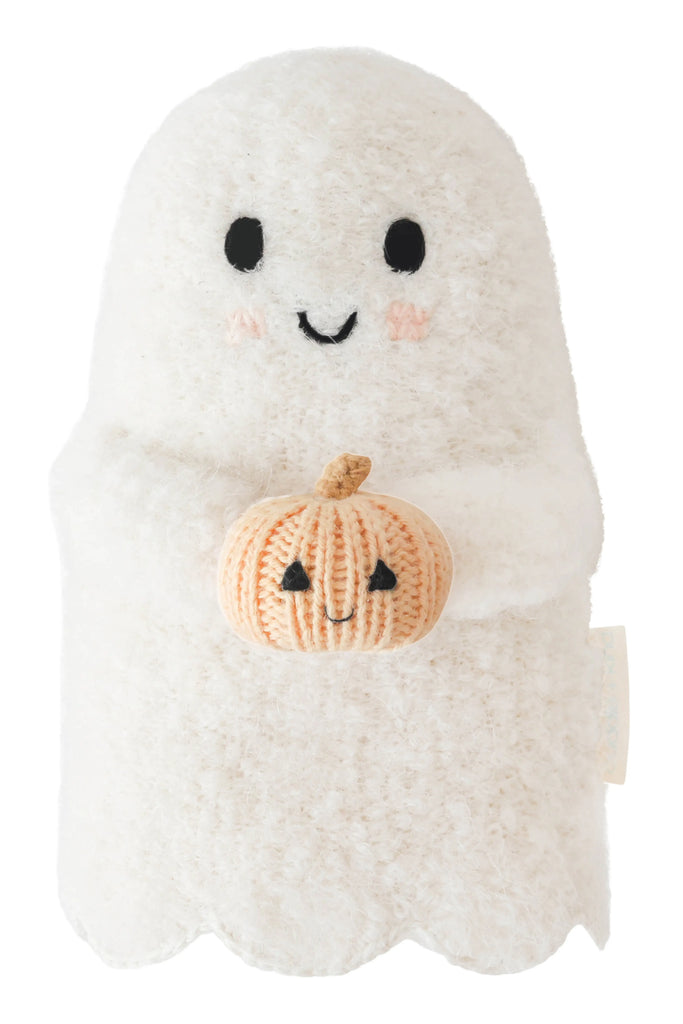 Cuddle + Kind Baby Ghost with Pumpkin is a plush, heirloom-quality ghost with a smiling face and blushing cheeks, holding a hand-knit orange and beige pumpkin, crafted from soft Peruvian cotton yarn.