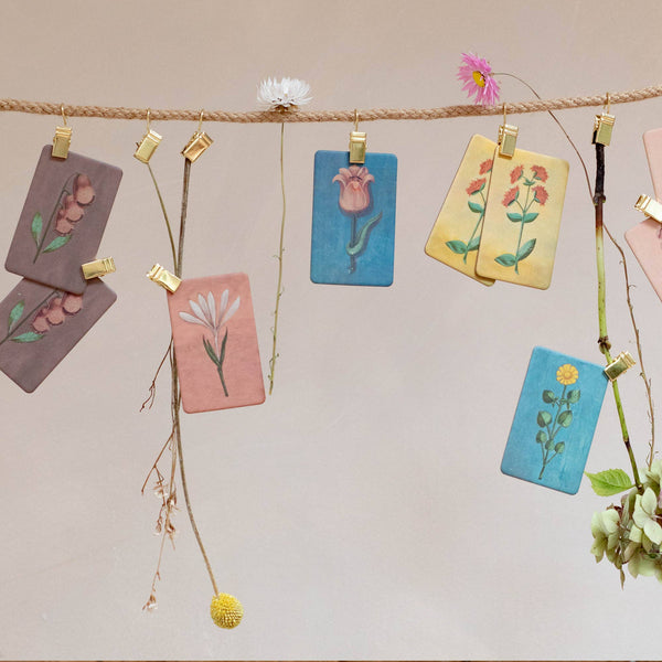 Hand-painted cards with watercolor flower illustrations are clipped to a rope with gold clips and fresh flowers, creating a charming display—perfect for featuring your Memory Game - Festival of Flowers.