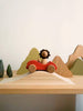 The Sabo Concept First Journey features a wooden lion riding in a red car on a shelf, with simple mountain and tree shapes—ideal for open-ended play and inspiring imagination.
