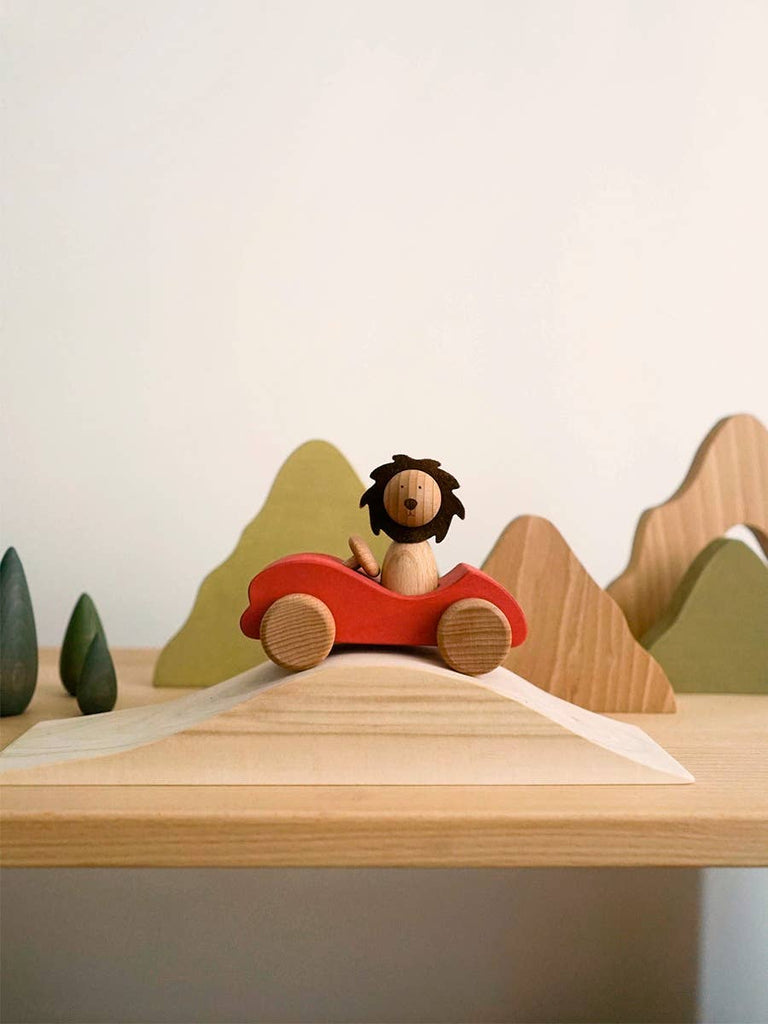 The Sabo Concept First Journey features a wooden lion riding in a red car on a shelf, with simple mountain and tree shapes—ideal for open-ended play and inspiring imagination.