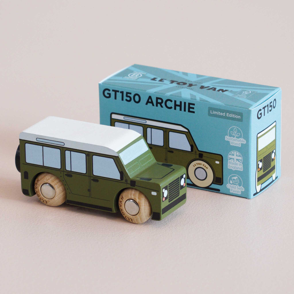 A small green classic toy car sits next to its blue box, labeled “No. 27 GT150 Archie | Made in England” with vehicle illustrations and limited edition details. Perfect for imaginative play, the toy features a white roof and wooden wheels, capturing the timeless charm of a beloved childhood collectible.