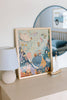 The Tales from the Deep 100 Piece Puzzle, framed and made from recycled materials, sits on a beige dresser by a white lamp and sailboat, with a round mirror and toy car reflected behind. Perfect for ages 5+.