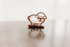 A small, sheep-shaped cookie cutter from the Farm Cutter Set - Eco Playdough Tool stands upright on a smooth surface, casting a soft shadow and reflection against a bright, blurred background.
