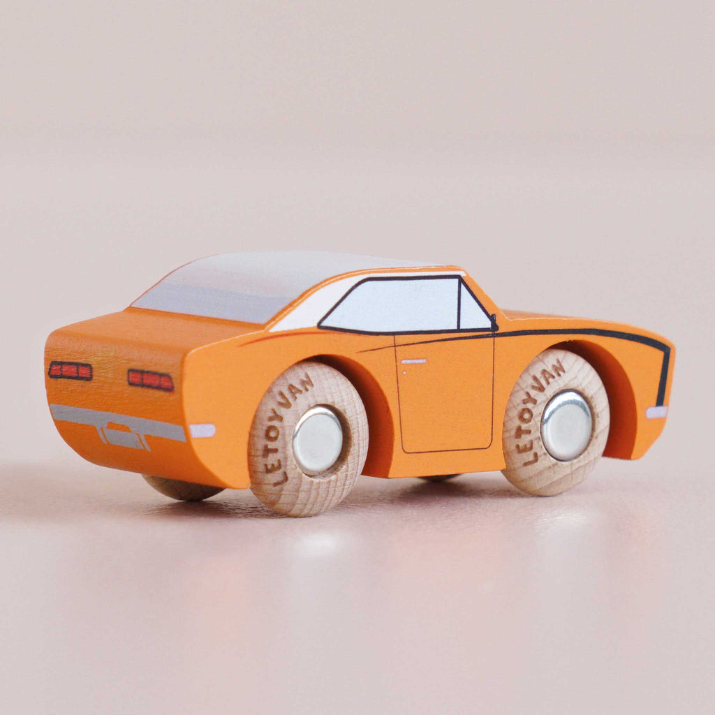 A small, orange wooden racing car with black accents and the name “No. 22 GT125 Cami | Made in England” printed on its wooden wheels sits on a light surface.