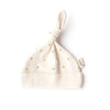 The Organic Baby Hat – Gold Sprig is a soft, cream-colored GOTS certified newborn hat made from organic cotton. It features a top knot, small yellow sprig prints, and a "oolie" fabric tag on the side, shown on a white background.