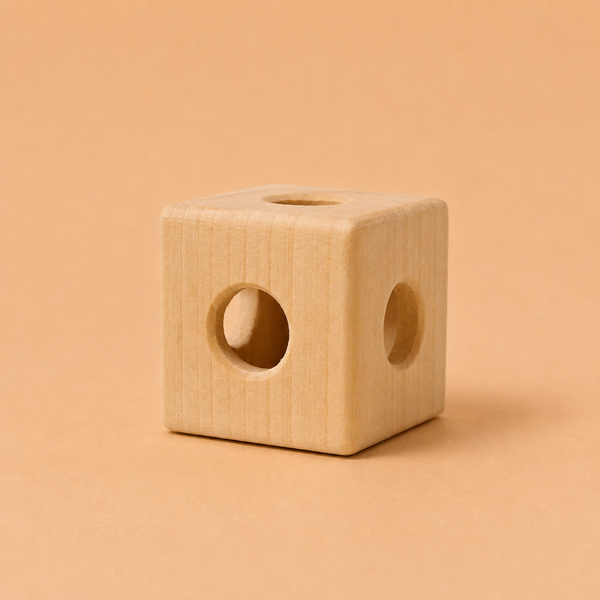 The Grimm’s Cube with Bell, a handcrafted natural wooden toy, features smooth edges and circular holes on each visible side and is displayed on a plain light brown background.
