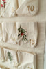 Close-up of the Sabo Concept Christmas Cotton Advent Calendar with gold-stitched numbers and botanical embroidery—red berries and green leaves—on pockets 14, 15, and 19. A charming holiday detail.