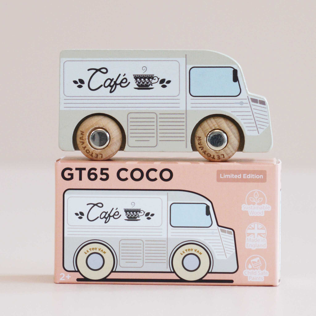 A wooden coffee van painted as a café, featuring “Café” and a cup design, sits atop its matching box labeled “No. 11 GT65 Coco | Made in England.” Perfect for thoughtful gifting, this charming toy encourages imaginative storytelling. The box displays logos for sustainable wood, made in England, and child-safe paints.