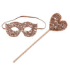 A pink sequin masquerade mask with an elastic band lies next to a matching pink sequin heart-shaped wand, perfect as a costume accessory for glamorous evenings, on a white background.