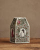 A paper lantern with embroidered bird and floral designs sits on a wooden surface beside the Coral & Tusk Birdhouse Tissue Box Cover, set against a plain beige background.