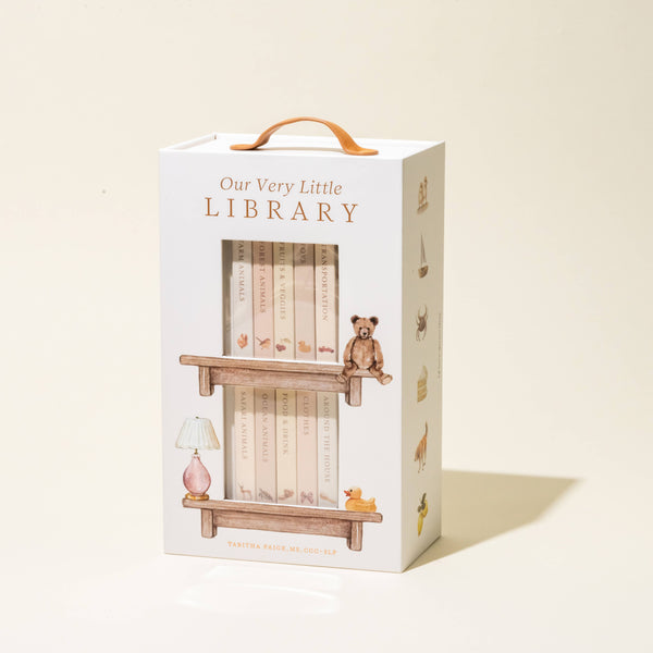 Our Very Little Library Board Book Set" comes in a white handled box adorned with illustrations of a toy bear, book-filled shelves, and small animals—ideal for introducing baby vocabulary and first words.