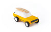 The Candylab Cotswold is a yellow toy car with a white roof and black wheels. Perfect for comfortable travel, this minimalistic design features a small wooden surfboard attached to the roof. The toy vehicle is set against a plain white background.