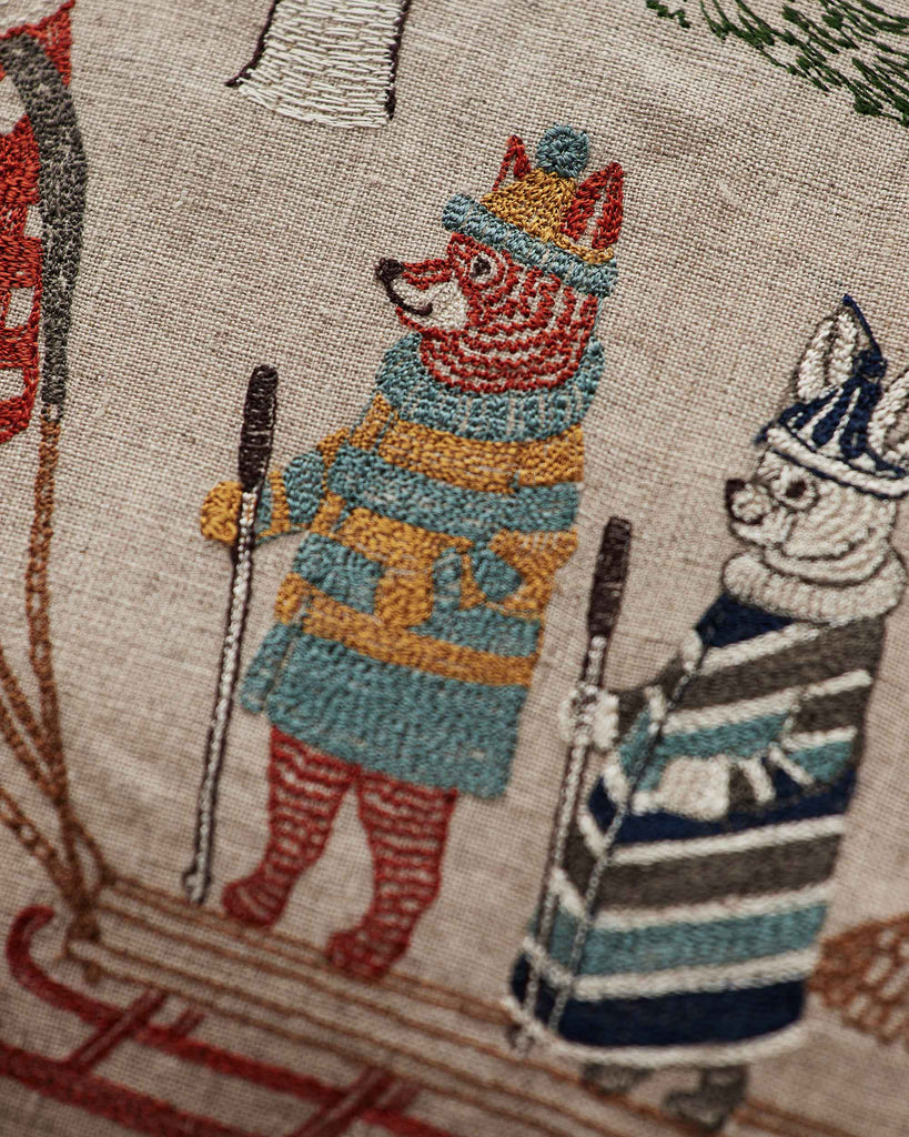 The Coral & Tusk Winter Fun Pillow features detailed embroidery of woodland animals, including a fox in a blue and yellow striped outfit with skis and ski poles, making it a whimsical holiday decor piece.