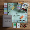 The Monopoly Vintage Bookshelf Edition is displayed on a wooden table, showcasing its iconic gray box and premium components, including money, property cards, houses, hotels, dice, tokens, and the classic game board.