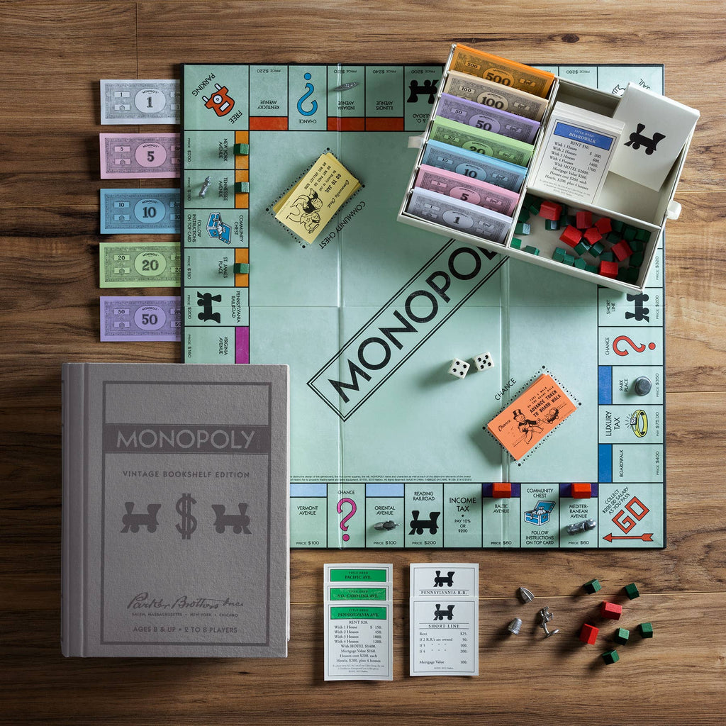 The Monopoly Vintage Bookshelf Edition is displayed on a wooden table, showcasing its iconic gray box and premium components, including money, property cards, houses, hotels, dice, tokens, and the classic game board.