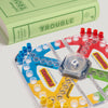 A close-up of the Trouble Vintage Bookshelf Edition game board shows colorful pegs and the Pop-O-Matic die roller, with the green book-shaped box labeled "Board Game: Trouble Vintage Bookshelf Edition" in the background.