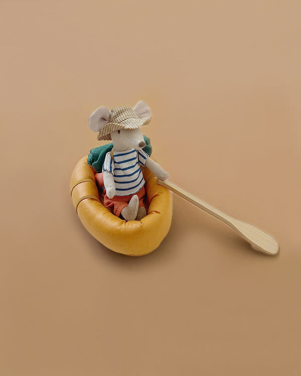 A Maileg Rubber Boat features a small stuffed mouse in a straw hat and striped shirt, holding a wooden paddle—ideal for hiker mice fans—set against a plain beige background.