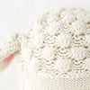 Close-up of a cream-colored, hand-knit Cuddle + Kind Lucy the Lamb doll with a raised bobble pattern and a touch of pink on the left side.