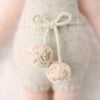 Close-up of Cuddle + Kind Ella the Unicorn, a handmade doll in a light outfit with two fluffy pastel-speckled pom-poms at the waist. The background is softly blurred.