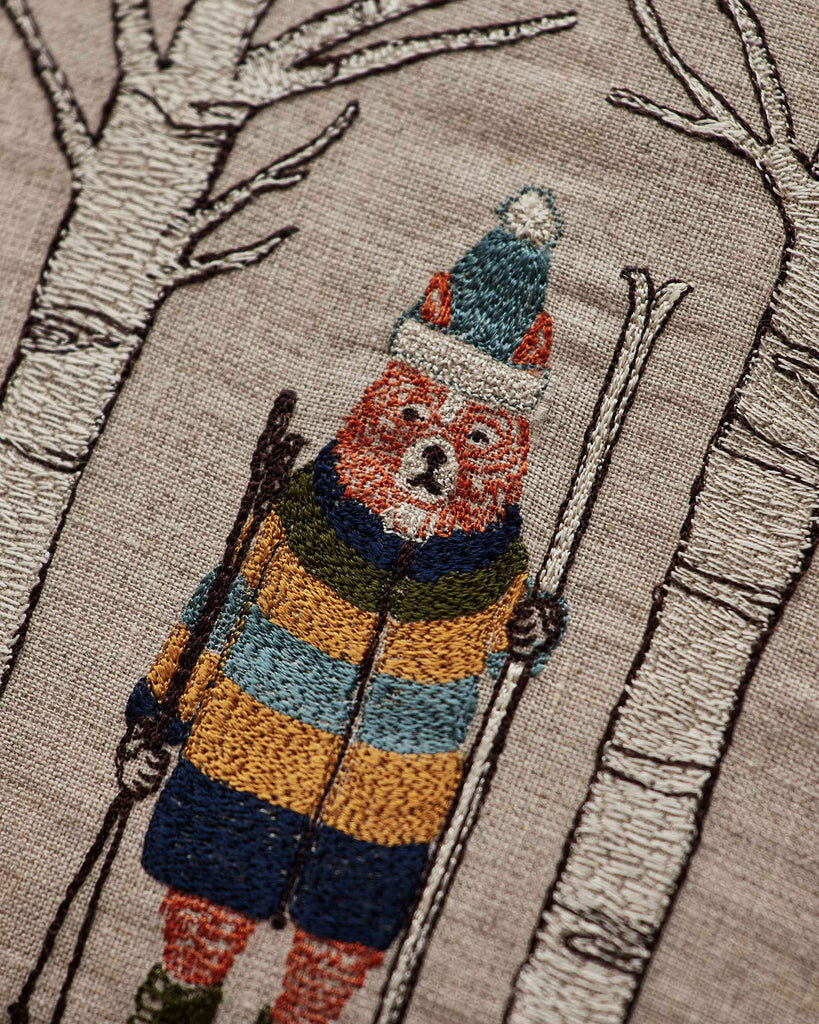 The Coral & Tusk Aspen Skiers Pillow features a fox in a striped winter coat and hat with ski poles, standing between two white-barked trees on beige fabric—a delightful embroidered accent for cozy winter decor.