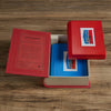 An open Board Book: Battleship Vintage Bookshelf Edition rests on a wooden surface, showing two blue game boards inside. The box lid features the Battleship logo, evoking the classic naval strategy game.