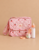 The Tiny Nurturers Set - Strawberry Picnic For Dolls is displayed, featuring a pink quilted nappy bag with strawberry patterns, a magic baby bottle, a small jar with a peach spoon, and a roll of tape, all arranged on a neutral background.
