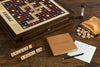 The Board Game: Scrabble Heirloom with Rotating Game Board features premium woods, letter tiles spelling words, an hourglass timer, score sheet with pencil, brown tile bag, and racks spelling "DELUXE" and "SCORE BG.