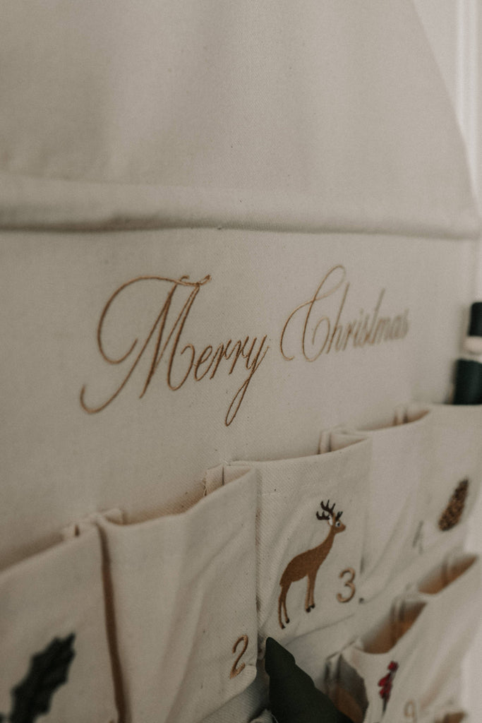 The Sabo Concept Christmas Cotton Advent Calendar features “Merry Christmas” in gold script, numbered pockets—some with festive images like a reindeer and pine cone—making it a charming embroidered holiday calendar.