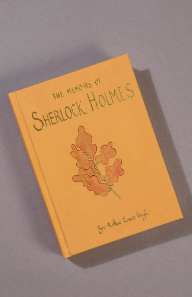 A collector's edition hardcover of "The Memoirs of Sherlock Holmes" by Arthur Conan Doyle showcases a yellow cover with an oak leaves illustration against a gray background.