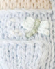 Close-up of Cuddle + Kind Tiny Bailey the Mouse, featuring light blue and cream knitted fabric, handmade in Peru, with a delicate embroidered white flower and green leaves.