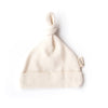 The Organic Baby Hat – Natural is a cream-colored, soft organic cotton hat for newborns with a folded brim, knotted top, and a small side tag, shown on a white background.
