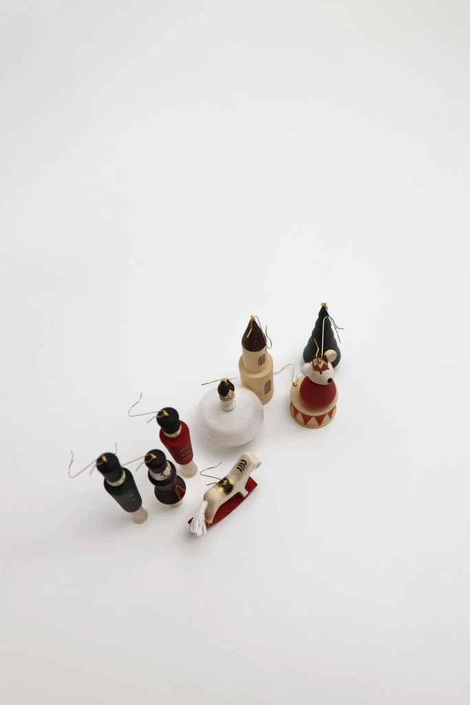 Seven small, hand-painted Sabo Concept Christmas Ornaments—featuring figures, a house, a sleigh, and trees—are displayed on a white background, perfect for enhancing your nutcracker ornament set.