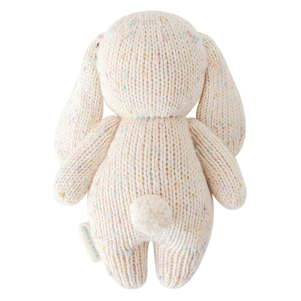 The Cuddle + Kind Baby Bunny - Confetti is a soft, hand-knit cotton yarn toy with long floppy ears, a round tail, and a light cream color with pastel speckles—shown from the back. Part of our charming cotton yarn collection.