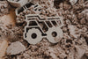A Construction Cutter Set - Eco Playdough Tool shaped like a dump truck rests on a surface covered with brown kinetic sand, surrounded by scattered shapes and chunks—perfect for sensory play with your favorite playdough tools.
