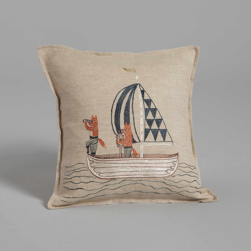 The Sailing Foxes Pillow is a beige square cushion featuring two playful foxes in a boat. One fox uses a telescope, while the other holds onto the rope of their striped and geometric-patterned sail, perfect for nautical-themed decor.