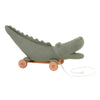 The Pull-Along Croc by Egmont Toys is a green knitted crocodile on a wooden wheeled base with a white pull string, designed to delight little ones and encourage the development of gross motor skills.