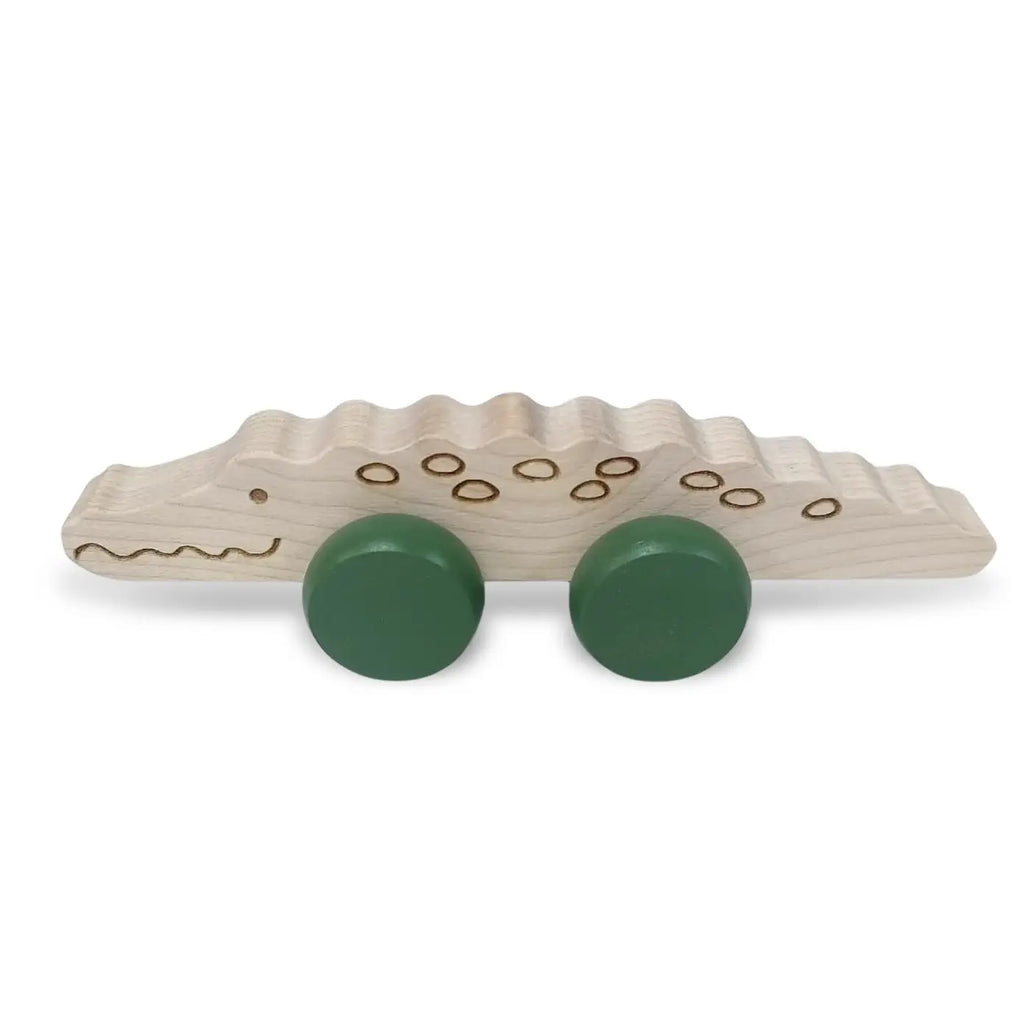 A Wooden Crocodile Push Toy with two green wheels attached. It features simple carved details for the eyes, nostrils, and body patterns, giving it a playful appearance. Designed as a fine motor skills toy, it's perfect for young children to push and pull.