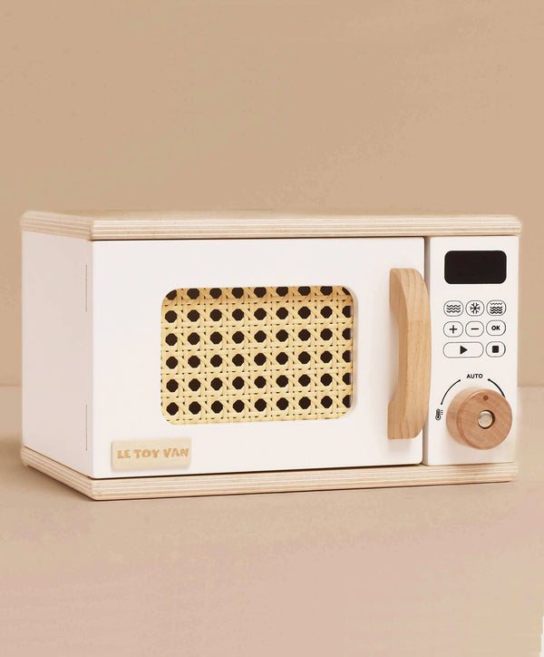 The Wooden Microwave (ships in one week) is a small, sustainable wood toy with a white body, natural handle and knob, woven rattan-look window, and a control panel featuring printed buttons and a digital display—perfect for play kitchens.