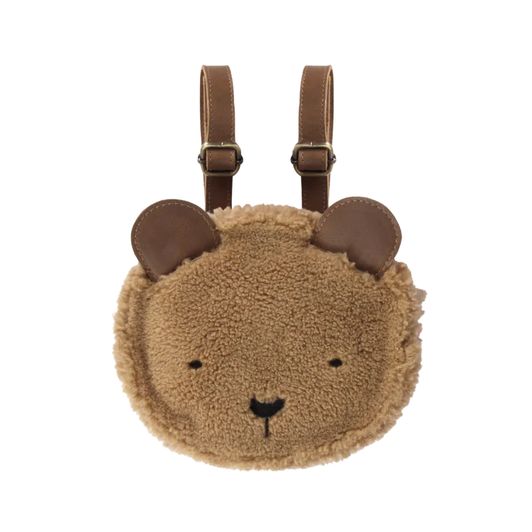 Circular brown faux shearling Donsje Pugi Backpack designed as a bear face with a smiling expression, ears at the top, and adjustable brown straps. The background is transparent.
