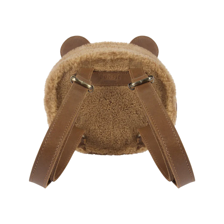 A brown Donsje Pugi Backpack | Bear with soft, plush faux shearling and premium leather straps, viewed from the back. The name "Donsje" is displayed on the top edge.