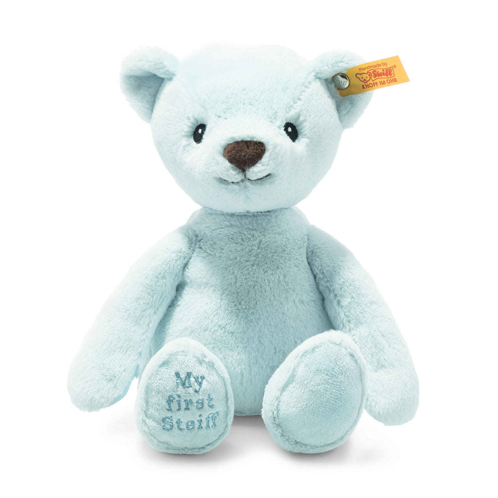 The My First Steiff Blue Teddy Bear, 10 Inches, is baby safe with a soft light blue fur, brown nose, yellow ear tag, and "My first Steiff" embroidered on its left foot. It sits upright and has a gentle, friendly expression.