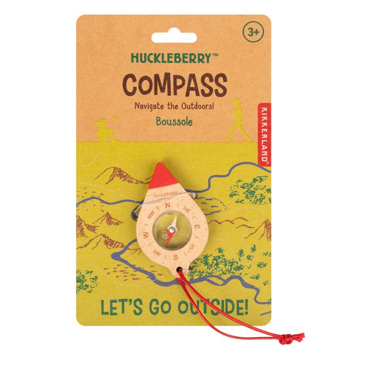 The Huckleberry Compass is an FSC beechwood compass for ages 3+, with a red tip and string, attached to map-themed packaging. Text on the pack reads "Navigate the Outdoors!" and "LET'S GO OUTSIDE!"—great for kids' outdoor fun.