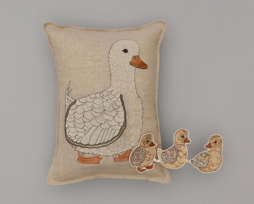 A Coral & Tusk Mama Duck Pocket Pillow featuring an embroidered Mama Duck followed by three removable ducklings on a neutral linen background. The embroidery is detailed, showing varied textures and shades.