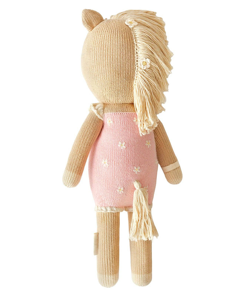 Cuddle + Kind Sophia the Pony is a fair trade, hand-knit doll horse plush with a light brown body, cream yarn mane and tail, wearing a pink dress with white spots. Handmade in Peru for unique charm; shown here from the back.