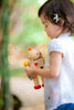 A young child with a flower in her hair stands outdoors, looking down with a gentle expression as she holds the Build-A-Robot toy, exploring its interchangeable heads to help learn about emotions.